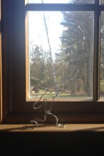 Figure of boy made of twisted wire in front of a window view of the forest.